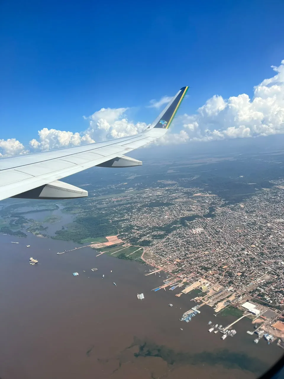 Asa do avião sobre um grande rio e a cidade vista do alto